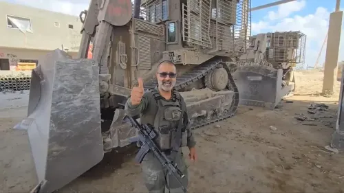 الحاخام زاربيف مبتسمًا أمام جرافة عسكرية، مع خلفية من المباني المدمّرة، يعكس دوره في هدم المنازل خلال العمليات العسكرية الإسرائيلية.