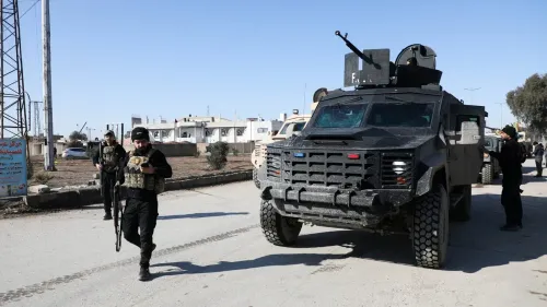 عناصر من قوات سوريا الديمقراطية يرتدون زيًا عسكريًا، يسيرون بالقرب من مركبة مدرعة في منطقة ذات أغلبية كردية شمال شرق سوريا.