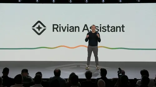 رجل يقدم مساعد Rivian الصوتي بالذكاء الاصطناعي أمام جمهور، مع شعار Rivian Assistant على الشاشة في عرض تقني.