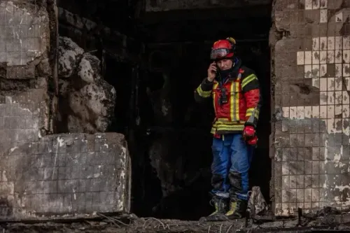 رجال الإطفاء يتحدثون عبر الهاتف وسط أنقاض مبنى سكني متضرر من هجوم بطائرات مسيرة في كييف، مما أسفر عن إصابات وحرائق.