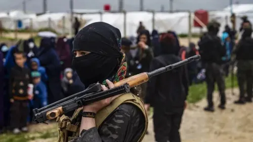 امرأة مسلحة ترتدي غطاء رأس أسود، تقف في مقدمة مجموعة من الأشخاص في مخيم، مما يعكس الأوضاع الأمنية في شمال سوريا بعد الاتفاقات الأخيرة.