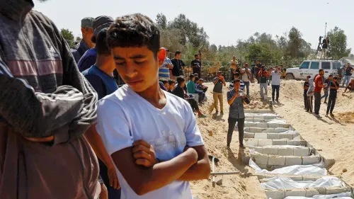 تجمع حشود من الأشخاص في موقع دفن جماعي في غزة، حيث يظهر صبي يبدو حزينًا وسط الحضور، مع التركيز على مشاعر الفقدان والأسى.