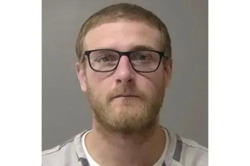 صورة لشون جريسون، ضابط شرطة متهم بالقتل، يرتدي نظارات وقميصًا مخططًا، مع تعبير جاد، في سياق محاكمة تتعلق بإطلاق نار مميت.