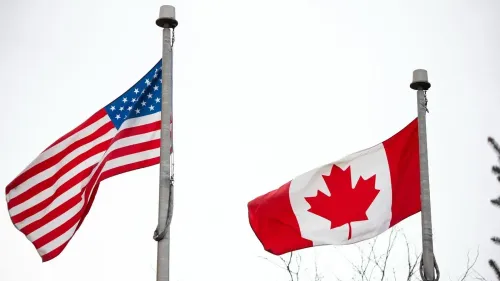 أعلام الولايات المتحدة وكندا ترفرفان على أعمدة، مع خلفية سماء رمادية، في سياق حادث إطلاق نار على القنصلية الأمريكية في تورنتو.