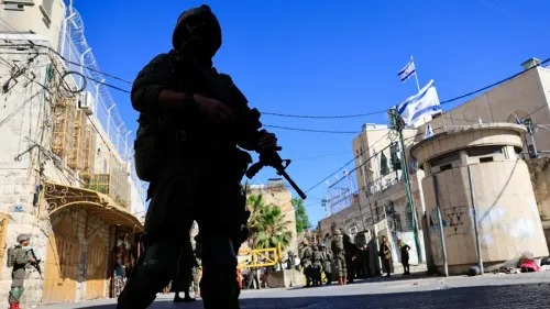 جنود إسرائيليون مسلحون يقفون في شوارع الخليل، مع وجود العلم الإسرائيلي في الخلفية، في سياق تصاعد التوترات حول الاستيطان.