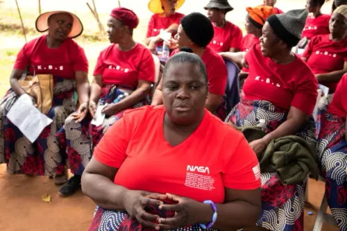 نساء يرتدين قمصان حمراء وتنانير مزخرفة، يجلسن في حلقة نقاش حول جمعية "Kuchemana" في هراري، زيمبابوي، حيث يتبادلن الأفكار لدعم المجتمع.