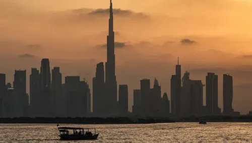 غروب الشمس خلف برج خليفة في دبي، مع قارب صغير يبحر في المياه، يعكس التحديات التي تواجه قطاع الشحن في ظل الأزمات الحالية.