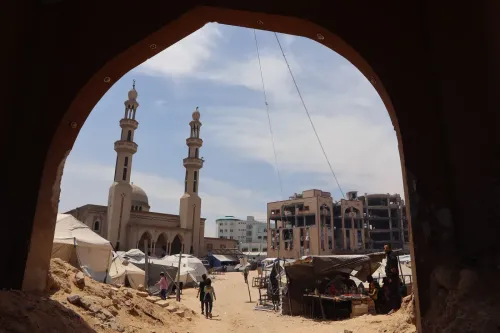 ساحة في غزة تضم خيامًا للنازحين، مع مسجد في الخلفية ومباني مدمرة، تعكس الأثر المدمر للصراع المستمر.