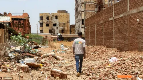 رجل يسير في منطقة مدمرة في السودان، حيث تظهر المباني المتضررة والأنقاض، مما يعكس آثار الحرب والأزمة الإنسانية المستمرة.