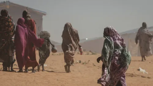 نساء سودانيات يرتدين أزياء تقليدية، يسيرن في مخيم للنازحين، تعكس معاناتهن في ظل الأوضاع الصعبة في دارفور.