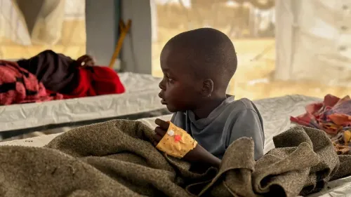 طفل سوداني يجلس في خيمة، يظهر عليه آثار الجروح، مما يعكس معاناة الأطفال في الحرب والنزاع المستمر في السودان.