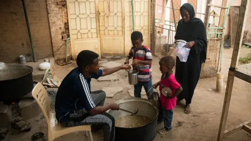 شخصان وطفلان في مطبخ مجتمعي في السودان، حيث يُعد الطعام وسط ظروف صعبة، يعكس أهمية التكايا في دعم الأسر خلال الأزمات.
