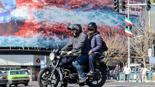 راكبان على دراجة نارية في مدينة إيرانية، مع خلفية تظهر لوحة إعلانات ملونة تعكس التوترات السياسية.