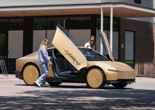 سيارة تسلا سايبركاب ذات الأبواب المفتوحة بتصميم مستقبلي ذهبي مع شخصين بجانبها في أوستن، تمهيداً لتوسيع خدمة الروبوتاكسي ذاتية القيادة.