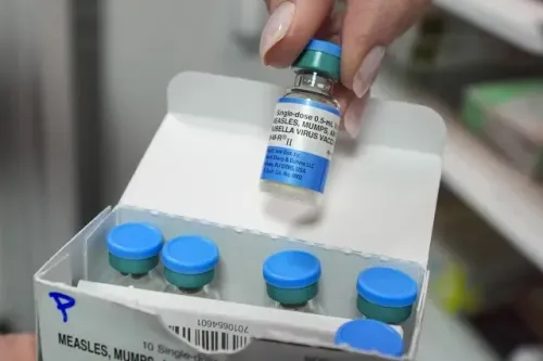 زجاجة لقاح الحصبة والنكاف والحصبة الألمانية تُرفع من علبة تحتوي على عدة زجاجات، مما يشير إلى أهمية التطعيم في الوقاية من تفشي المرض.
