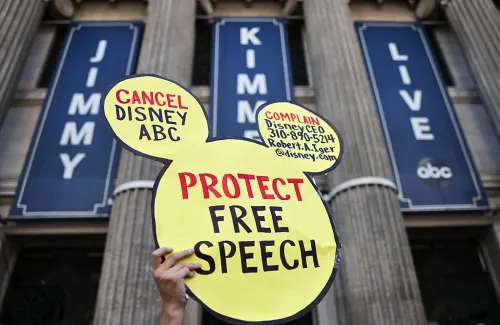 شخص يحمل لافتة على شكل أذني ميكي مكتوب عليها "حماية حرية التعبير" أمام مبنى برنامج Jimmy Kimmel Live على قناة ABC، تعبيراً عن احتجاجات ضد ديزني وتركيز ملكيتها الإعلامية.