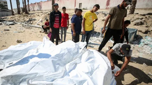 مجموعة من الأشخاص الفلسطينيين يتجمعون حول جثث مغطاة بأقمشة بيضاء في غزة، مما يعكس آثار الصراع والدمار المستمر.