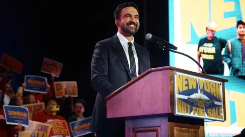 زهران ممداني يتحدث في مناسبة انتخابية في نيويورك، مع لافتات مؤيدة في الخلفية، داعمًا سياسات تقدمية مثل إلغاء أجرة الحافلات.