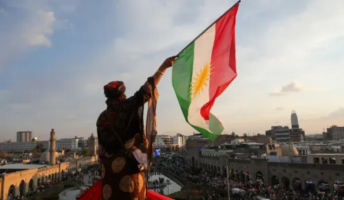 متظاهر كردي يرفع العلم الكردي في تجمع حاشد بأربيل، معبرًا عن التضامن ضد الهجمات العسكرية السورية.