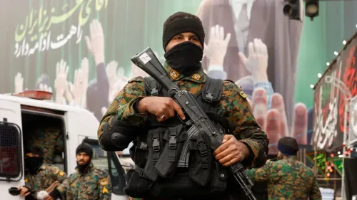 عناصر من القوات الإيرانية يرتدون زيًا عسكريًا ويحملون أسلحة، يقفون أمام جدارية تحمل شعارات وطنية تعكس التوترات الحالية في المنطقة.