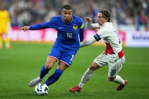 مبابي يتقدم بالكرة خلال مباراة كرة قدم، بينما يحاول لاعب آخر من الفريق المنافس اعتراضه. الصورة تعكس حماس المنافسة قبل كأس العالم 2026.