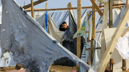 رجل يقف داخل مخيم مؤقت في المواصي بجنوب غزة، محاط بخيام ممزقة، مما يعكس معاناة الأسر النازحة في ظل استمرار النزاع.