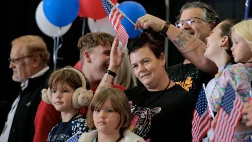 مجموعة من الأشخاص يحملون أعلام الولايات المتحدة في احتفال، مع وجود بالونات ملونة في الخلفية، يعكس الأمل في إعادة توطين اللاجئين.