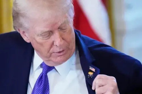 ترامب ينظر إلى دبوس يحمل صورته الكاريكاتورية، مثبتًا على طية صدر سترته بجانب دبوس العلم الأمريكي، خلال فعالية في البيت الأبيض.