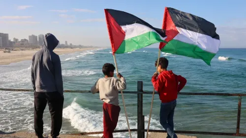 أطفال فلسطينيون يحملون الأعلام الفلسطينية على شاطئ غزة، يعبرون عن التضامن في ظل الأوضاع السياسية الصعبة.