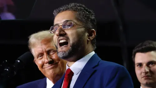 عامر غالب، عمدة هامترامك، يتحدث خلال حدث سياسي مع ترامب خلفه، مع التركيز على قضايا العلاقات الخارجية والتحديات التي تواجهه.