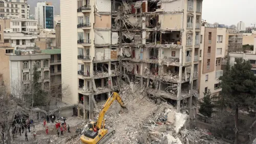 مبنى سكني مدمّر جزئيًا في طهران، مع وجود جرافة وعمال إنقاذ في الموقع، يعكس آثار الصراع والتوترات الجيوسياسية في المنطقة.