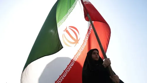 امرأة ترتدي الحجاب تحمل علم إيران، مما يعكس الأجواء الوطنية والتوترات الإقليمية في سياق الحرب على إيران وتأثيراتها.