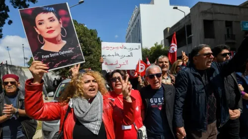 محتجون في تونس يرفعون لافتات تطالب بالإفراج عن الصحفية سونيا دحماني، مع تواجد أعلام تونسية في الخلفية، تعبيراً عن قمع الحكومة.