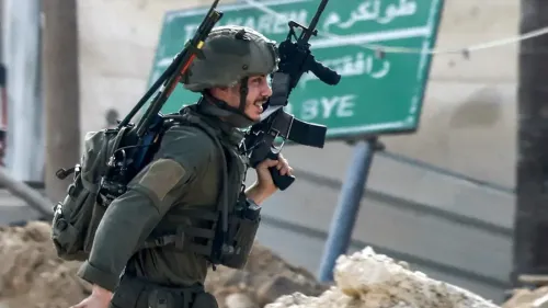 جندي إسرائيلي يحمل سلاحه أثناء تحركه في منطقة حضرية، مع لافتة خلفية تشير إلى موقعه.
