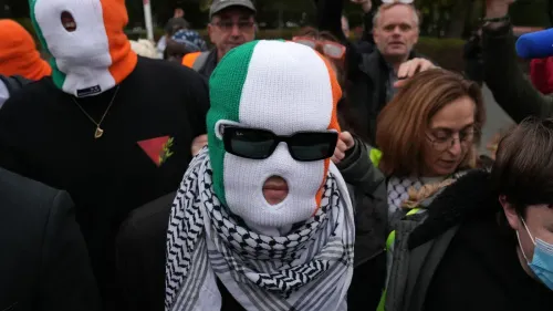 شخص يرتدي قناعًا مزينًا بألوان علم أيرلندا ونظارات شمسية، وسط حشد من المتظاهرين في حدث يعبر عن التضامن مع فلسطين.