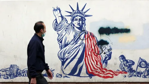 رجل يسير بجوار جدارية تمثل تمثال الحرية مع علم أمريكي ممزق، تعبيراً عن التوتر بين الولايات المتحدة وإيران.