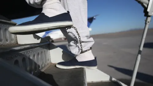 رجل يرتدي ملابس رمادية وسلسلة على كاحله، يصعد إلى الطائرة، في سياق عمليات ترحيل الفلسطينيين من الولايات المتحدة إلى إسرائيل.