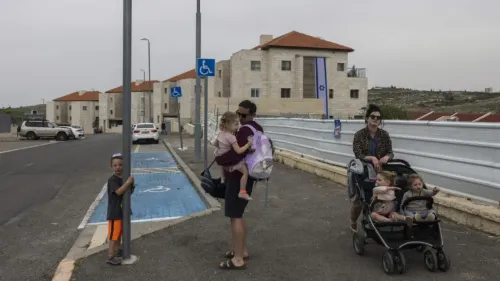عائلة إسرائيلية تتجول في مستوطنة بالضفة الغربية، مع وجود لافتات تشير إلى خدمات قنصلية جديدة للمستوطنين.