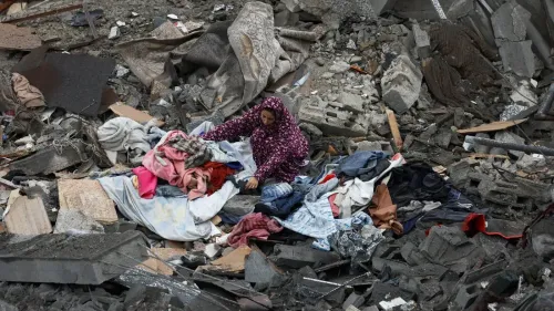 امرأة ترتدي عباءة تتفقد الملابس المبعثرة بين أنقاض المباني المدمرة في غزة، تعبيراً عن معاناة السكان بعد الصراع.