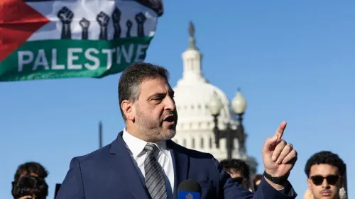 أسامة أبو إرشيد يتحدث أمام مبنى الكابيتول الأمريكي مع رفع علم فلسطين خلفه، في سياق دعم الحقوق الفلسطينية والعدالة القانونية.