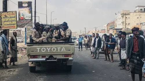 عناصر مسلحة في شاحنة تويوتا في أحد شوارع اليمن، بينما يتجمع المدنيون حولهم، يعكس الوضع الأمني المتوتر في المنطقة.