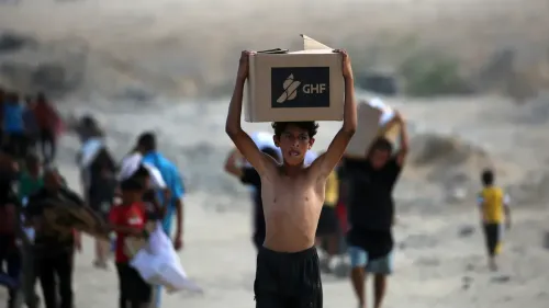 طفل يحمل صندوق مساعدات من مؤسسة GHF وسط مجموعة من الأشخاص في غزة، مما يعكس الأوضاع الإنسانية الصعبة في المنطقة.