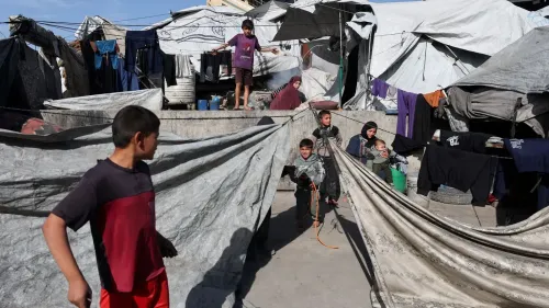 أطفال يلعبون في مخيم للاجئين في غزة، حيث تظهر الخيام والملابس المعلقة في الخلفية، مما يعكس الظروف المعيشية الصعبة.