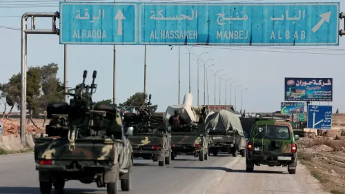 قافلة من المركبات العسكرية تسير على طريق في سوريا، مع لافتات تشير إلى الاتجاهات نحو الرقة والحسكة ومنبج.