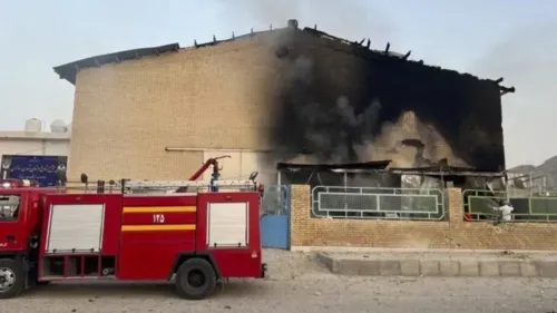 قاعة رياضية في إيران تعرضت لأضرار جسيمة نتيجة ضربة صاروخية، مع وجود دخان يتصاعد من السقف المحترق، بينما تتواجد سيارة إطفاء بالقرب.