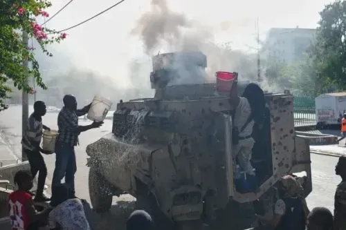 مدنيون وضباط شرطة يسكبون الماء على سيارة شرطة مدرعة تتصاعد منها الدخان بعد هجوم عصابة في بورت أو برنس، هايتي.