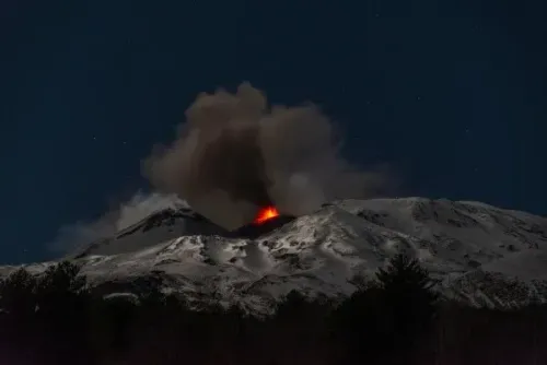 ثوران بركان جبل إتنا في صقلية، مشهد ليلي يظهر تدفقات الحمم البركانية والدخان يتصاعد من القمة المغطاة بالثلوج.