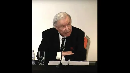 وليد الخالدي، المؤرخ الفلسطيني البارز، يتحدث في ندوة، مع زجاجة ماء وملاحظات أمامه، مستعرضًا تأثيره في التأريخ الفلسطيني.