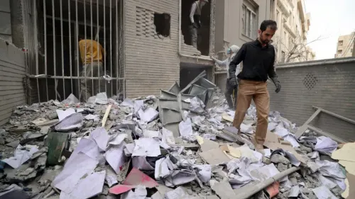 رجل يمشي بين أنقاض مبنى مدمر، محاط بأوراق ممزقة وحطام، يعكس آثار النزاع في المنطقة.