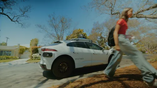 سيارة ذاتية القيادة من Waymo متوقفة في حي سكني بينما يمر مراهق يحمل حقيبة ظهر، تعبير عن توسع الخدمة للمراهقين في ناشفيل.
